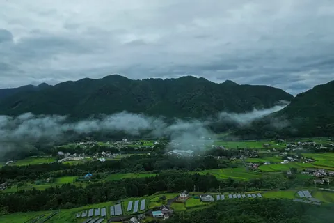 雲霧が流れる山間の農村を上空から望む